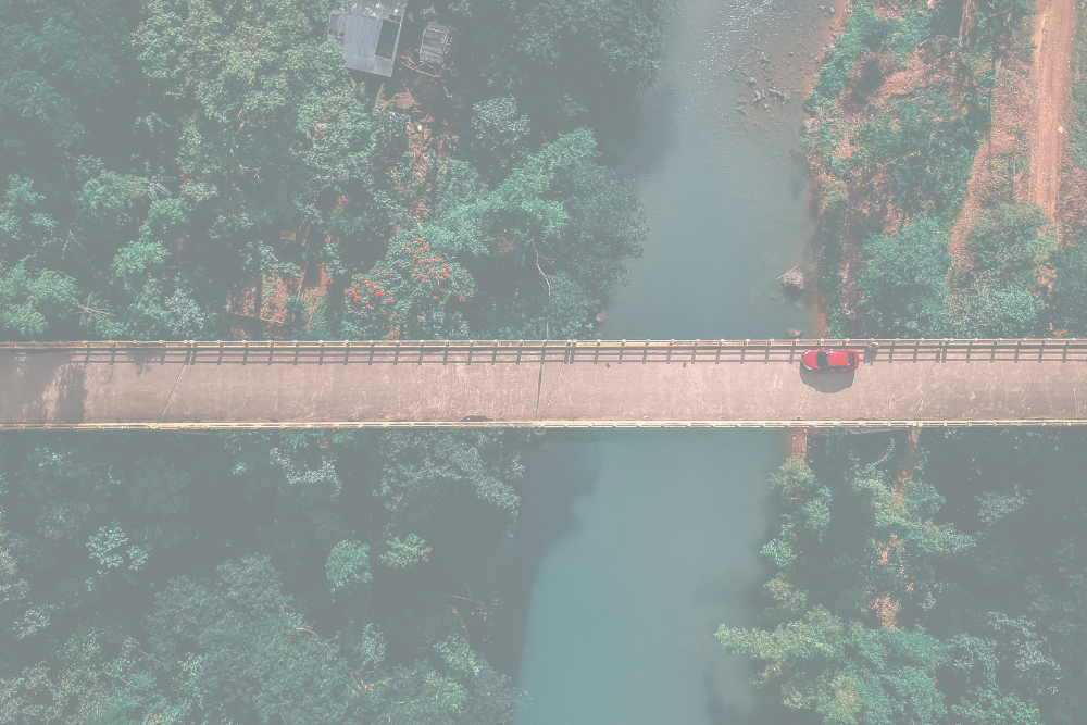 An image from above, showing a bridge crossing a body of water surrounded by trees.